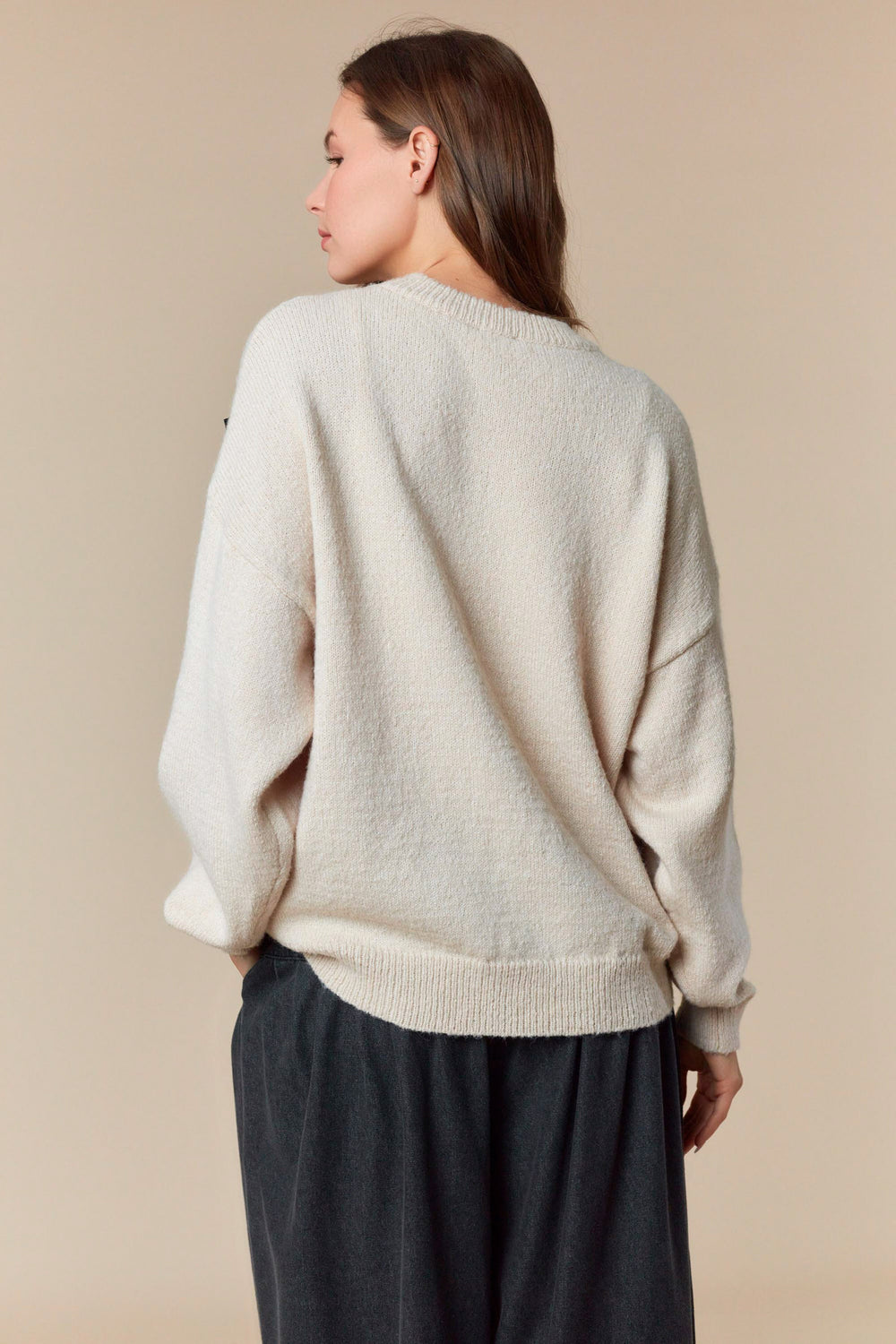 Woman wearing a beige sweater and dark pants against a beige background