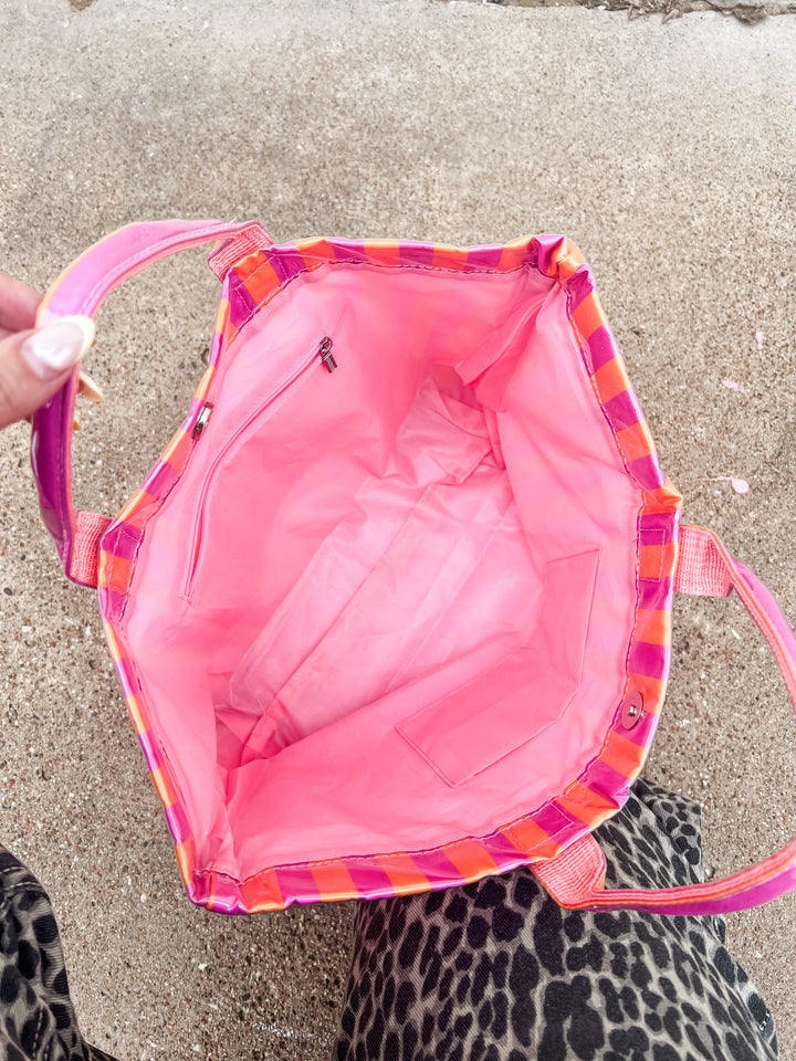inside view of pink and orange striped bag with colorful trim held by a hand on a concrete surface