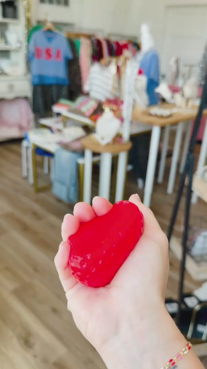 hand squeezing a red strawberry squishy sensory toy inside a boutique