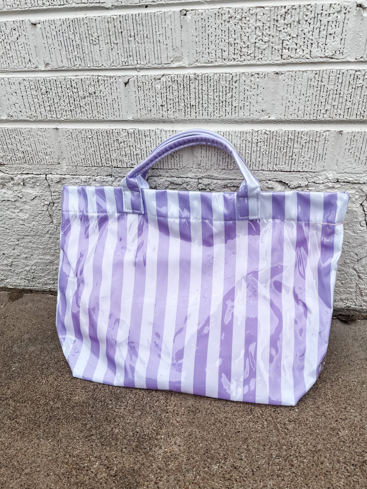 Purple and white striped tote bag on a concrete surface with a stone wall background