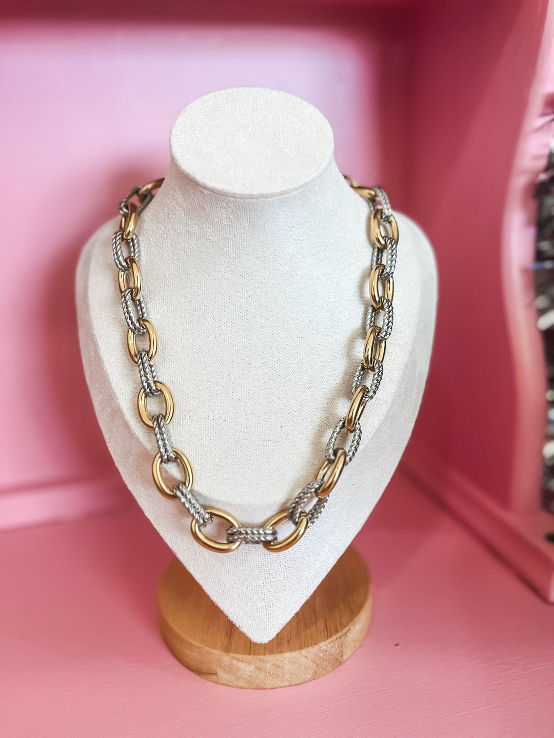 A two-tone chain necklace with gold and silver links, displayed on a white jewelry bust against a pink background.