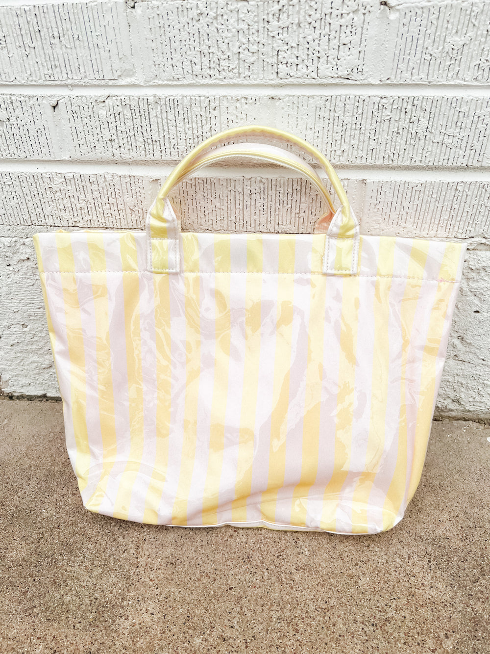 Yellow and white striped tote bag on a concrete surface with a light white brick wall background